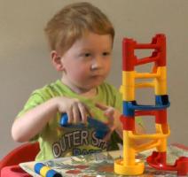 Toddler sitting erect on a chair building a marble run.